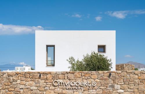 a white house behind a stone wall at Omvrodektis Village in Mykonos Airport