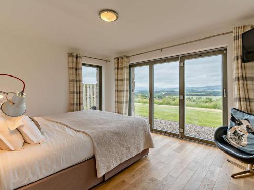 a bedroom with a bed and a chair and windows at 2 Bed in Forfar oc-92621 in Aberlemno