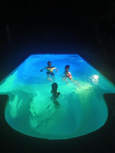 three people swimming in a pool at night at Hôtel-bungalows La Pirogue in Sambava