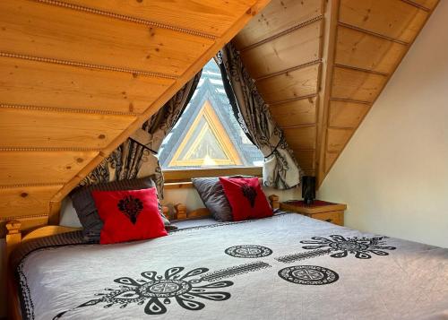 a bedroom with a bed with red pillows and a window at Domki Pod Góralskim Niebem in Zakopane