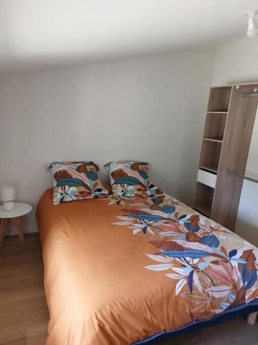 a bed with an orange comforter and two pillows at Gîte La Caillère in Moncoutant