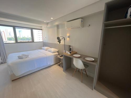 a white bedroom with a bed and a desk and a chair at Manaíra Apart Hotel in João Pessoa