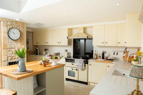 a kitchen with white cabinets and a clock on the wall at The Cottage - Elegant 3 Bedroom Cottage in the Heart of Stow-on-the-Wold in Stow on the Wold