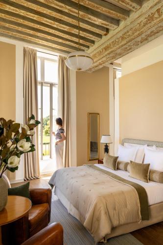 a woman standing in a bedroom looking out the window at Château d'Augerville Golf & Spa Resort - TemptingPlaces Collection in Augerville-la-Rivière