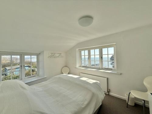 a white bedroom with a bed and two windows at 1 East Cliff in Lyme Regis
