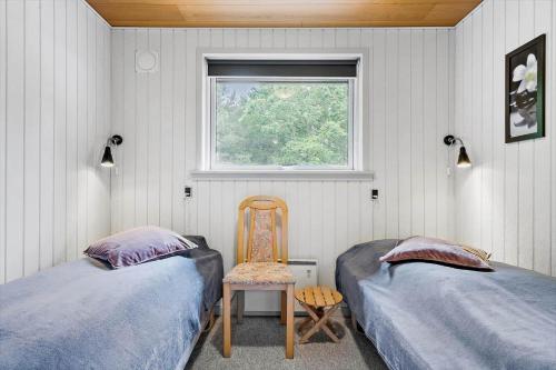 a bedroom with two beds and a chair and a window at 198-Ringkobing-Bogealle-8 in Nørby