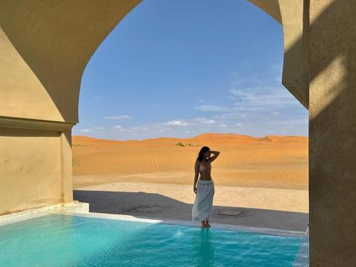 a woman standing next to a pool of water in the desert at Sinbad Merzouga Camp in Merzouga
