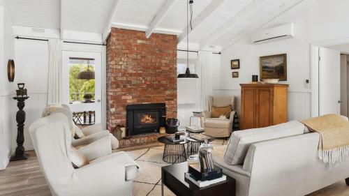 a living room with white furniture and a brick fireplace at Malmsbury Cottage in Malmsbury