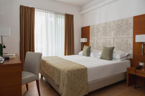 a bedroom with a bed and a desk and a window at Hotel Daniele in Lignano Sabbiadoro