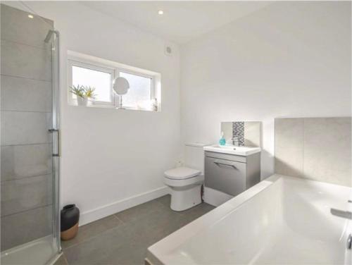 a bathroom with a tub and a toilet and a window at Artsy Minimalist Suite in Southend-on-Sea