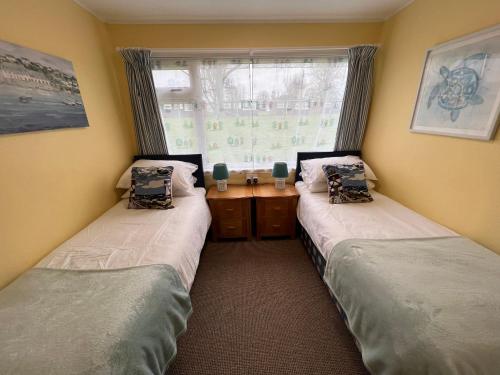 two twin beds in a room with a window at 'Sunnyside' Chalet, walk to the beach & close to Norfolk broads - pet friendly! in Great Yarmouth