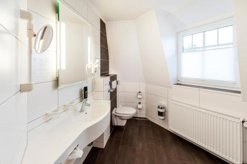 a white bathroom with a toilet and a sink at Hotel Hilker in Bersenbrück
