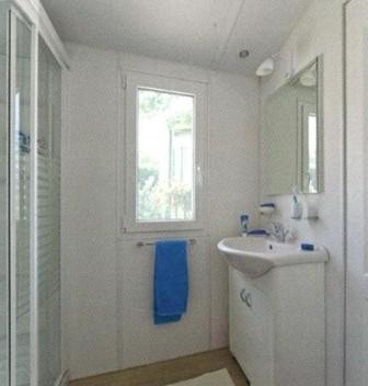 a white bathroom with a sink and a blue towel at Flower Camping Le Pont du Tarn in Florac
