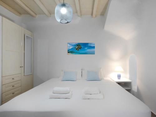 a white bedroom with a large white bed with blue pillows at Parfait Villa, Mykonos in Agios Ioannis Mykonos