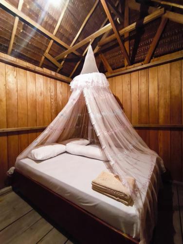 a bed in a wooden room with a mosquito net at Nadi awin kamam in Fambemuk
