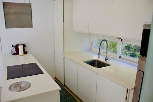 a kitchen with white cabinets and a sink and a window at White and Light House in Costa da Caparica