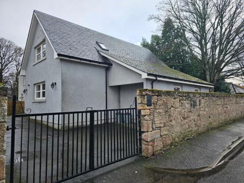 a white house with a fence and a stone wall at The Wee Corsee Cosy Coastal Cottage in the Heart of Nairn in Nairn