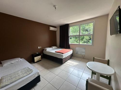 a room with two beds and a table and a window at Hotel Guaporé - Campo Bom RS in Campo Bom