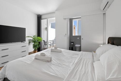 a white bedroom with a bed and a flat screen tv at Top Floor Penthouse with Valletta Views & Terrace in Gwardamanġa