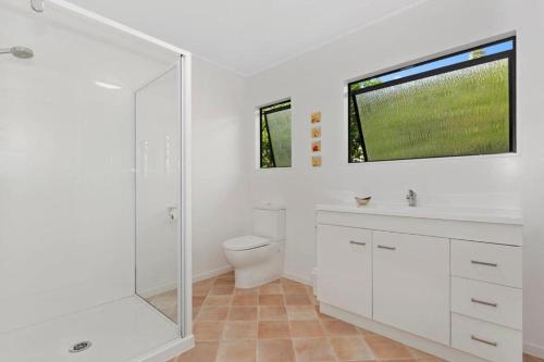 a white bathroom with a toilet and a window at Spectacular Woolleys Bay in Matapouri