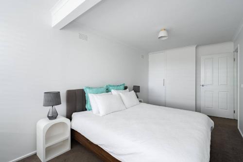 a white bedroom with a white bed and a lamp at 550m to Beach, SPA and Large Backyard , Sleep 9 in Ocean Grove