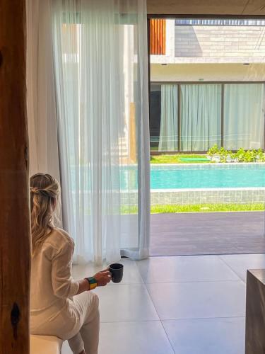 a woman sitting on a chair looking out of a window at Brisa e Sal in São Miguel dos Milagres