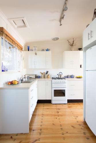 a white kitchen with white appliances and wooden floors at Sunset Over Sea Little Beachside Villa Rosebud McCrae in Rosebud