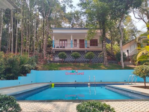 a villa with a swimming pool in front of a house at Green Leaf in Padinjarathara