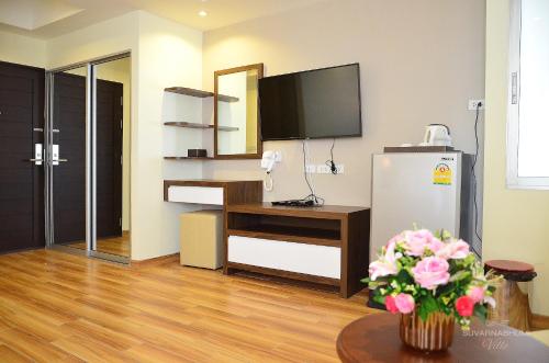 a living room with a television and a table with flowers at Suvarnabhumi Ville Airport Hotel in Lat Krabang