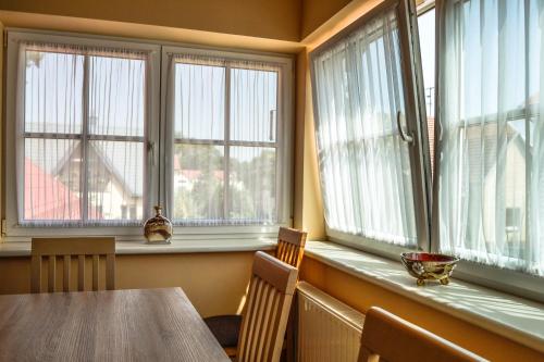 a dining room with a table and three windows at Vila Liepa in Birštonas