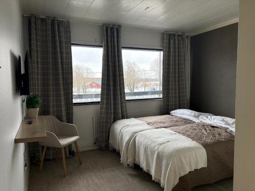 a bedroom with a bed and a desk and two windows at Hotel Sommarvind in Inkoo