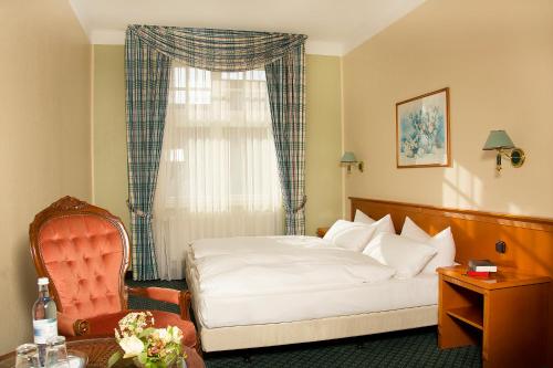 a bedroom with a bed and a chair and a window at Hotel Kronprinz in Greifswald