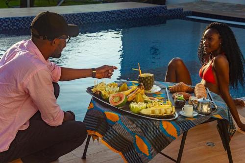 a man and a woman sitting at a table with a tray of food at GINFORM at Hotel Petit Brussel in Lomé