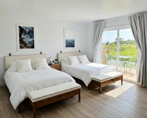 a white bedroom with two beds and a balcony at Motel Seal Rock in Perce
