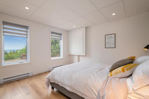a white bedroom with a bed and a window at Käbane Horizon Boréal - Le Belvédère in Les Éboulements