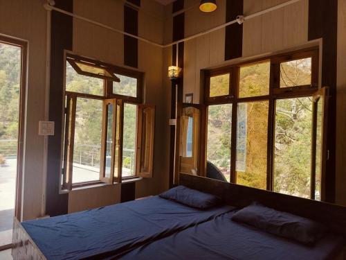 a bedroom with windows and a bed with blue sheets at Amritganga Homestay in Uttarkāshi
