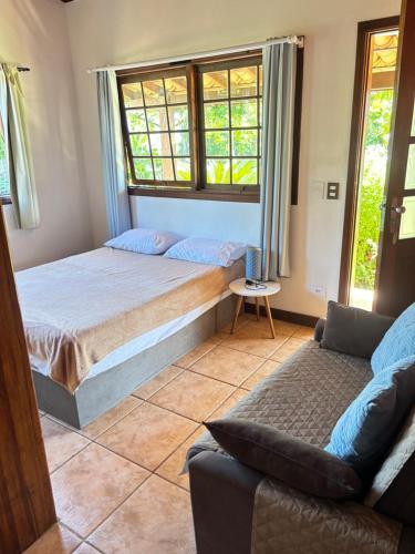 a bedroom with a bed and a couch and windows at Micas House in Ilhabela