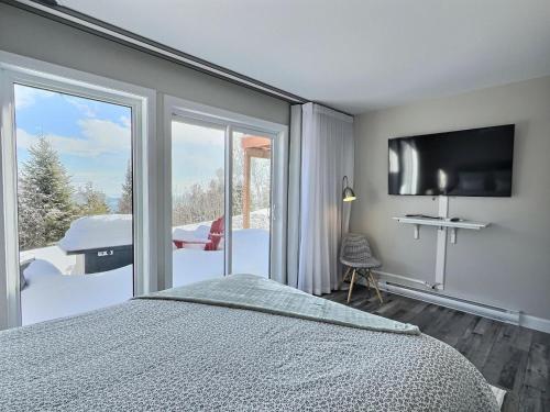 a bedroom with a bed and a tv and a balcony at Käbane Miramar - L'Oasis du Fleuve in Les Éboulements