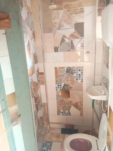 a bathroom with a toilet and a mosaic wall at Casa em Araruama com 3 quartos e muito arejada in Araruama