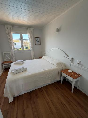 a white bedroom with a large bed and a table at Apartamento Cala En Bosch B10 in Cala en Bosc