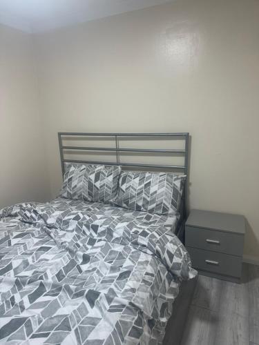 a bed with a gray and white comforter and a night stand at Godwinning lodge in Thamesmead