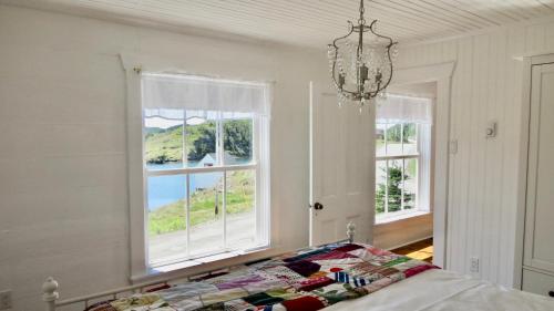 a bedroom with two windows and a bed and a chandelier at The Old Salt Box Co. - Evelyn's Place in Herring Neck