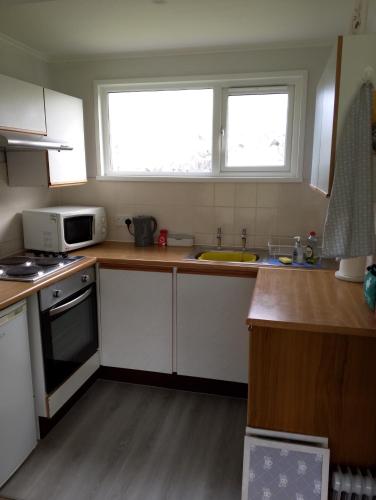 a kitchen with white cabinets and a sink and a microwave at The Warren Chalet in Cromer