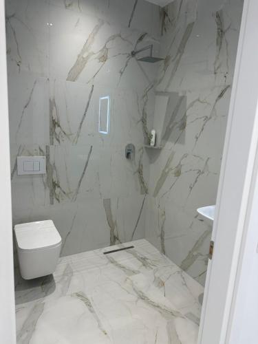 a white bathroom with a toilet and a marble wall at Qyteza guest house in Shkodër