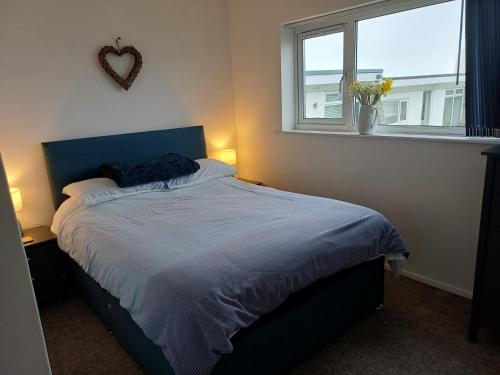 a bedroom with a bed with a blue headboard and a window at Chalet 18 Widemouth Bay Holiday Village in Bude