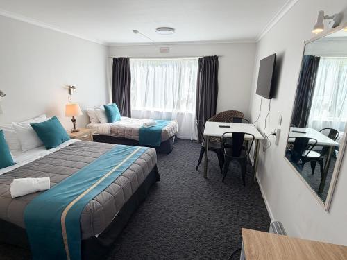 a hotel room with two beds and a desk at Champers Motor Inn in Lower Hutt