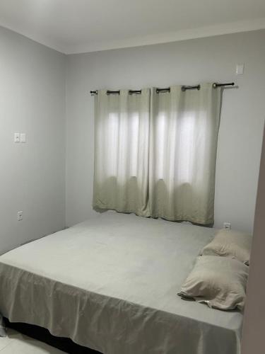 a white bedroom with a large bed with a window at Casa com 3 quartos aconchegante in Anápolis