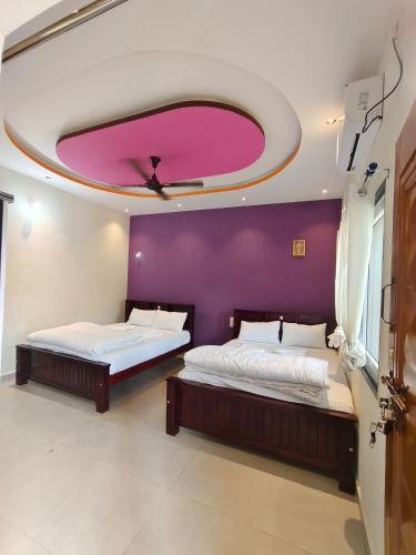 two beds in a room with a purple wall at NARGILA HAMPi in Hampi