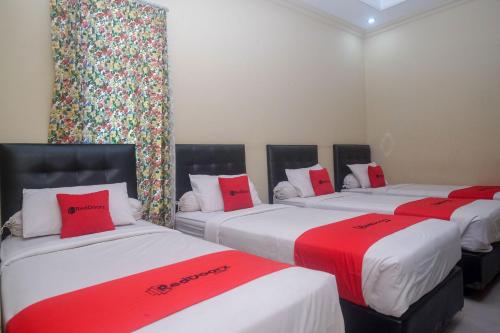 three beds in a room with red and white pillows at RedDoorz Plus @ Timoho in Yogyakarta