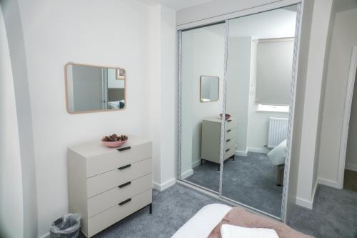 a white bedroom with a mirror and a dresser at Little Haven Thames view Free Parking Closer to Heathrow in Staines